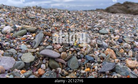 Struktureller Hintergrund aus Strandkieseln, Felsen und Sand entlang der Strandlinie eines geschützten kornischen Strandes. Stockfoto