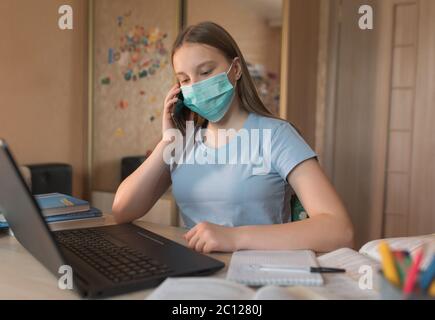 Teenager Mädchen, in einer medizinischen Maske, Desinfektion von Bakterien und Keimen und Viren, Anrufe auf einem Smartphone, Laptop-Monitor, E-Education und Internet Stockfoto