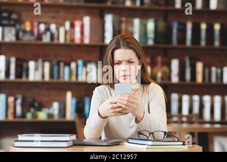 Aufgeregt Mädchen lesen lästige Nachrichten auf Handy im Café Stockfoto
