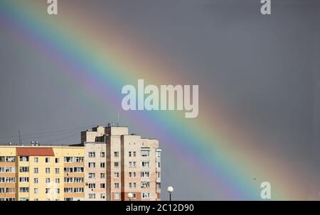 Heller, mehrfarbiger, breiter, farbenfroher Regenbogen nach dem Sturm am grauen Himmel über den Stadthäusern Stockfoto