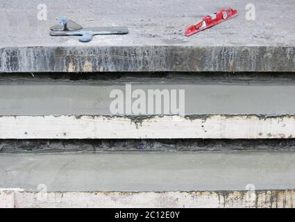 Werkzeuge: Zwei Kelle, Ebene auf den Stufen und Holzschalung mit Betonmischung gefüllt. Stockfoto