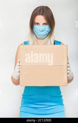 Lieferung während des Coronavirus-Ausbruchs. Speicherplatz kopieren. Frau halten Karton in medizinischen Gummihandschuhen und Maske auf weißem Hintergrund. Online-Shopping und Stockfoto