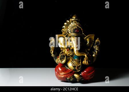 Eine isolierte Skulptur des indischen gottes Ganesha auf einem reflektierenden weißen Tisch in einem dunklen Hintergrund platziert Stockfoto