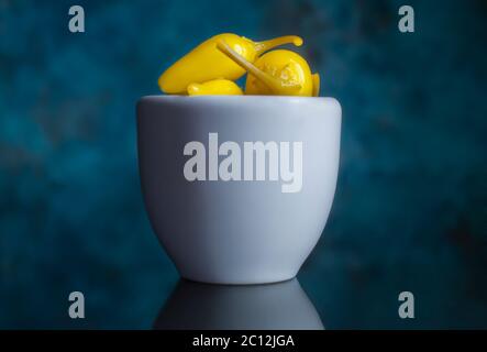 Pepperoncini Paprika in einer weißen Tasse mit blauem Hintergrund und auf einer reflektierenden Oberfläche, Makrofotografie Stockfoto
