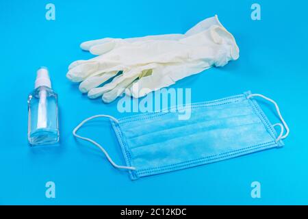 Horizontale Draufsicht auf neue Hygieneartikel, bestehend aus weißen Latexhandschuhen, Gesichtsmaske und Handdesinfektionsmittel auf blauem Hintergrund Stockfoto