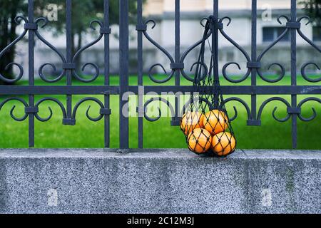 Schwarze Netztasche voller Orangen als Symbol für Null Abfall Lebensstil hängt auf dem schmiedeeisernen Zaun Stockfoto