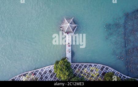 Luftaufnahme von oben nach unten auf der chinesischen kleinen Pagode am blauen See mit Menschen, die auf einer Brücke zur Pagode gehen. Stockfoto