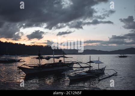 Traditionelle philippinische Fischerboote dockten in einer Bucht während des wunderschönen Sonnenuntergangs in El Nido Palawan auf den Philippinen an Stockfoto