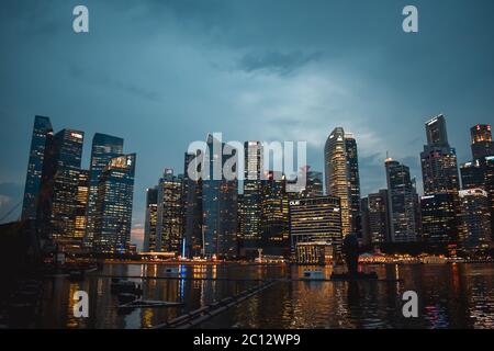 Abendfoto des beleuchteten Handelsviertels von Singapur, das sich in der Abenddämmerung im Wasser der Bucht widerspiegelt Stockfoto