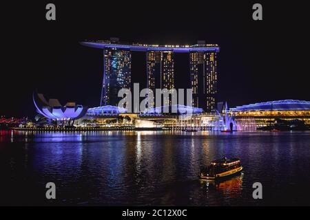 Touristenboot in der Singapore Bay vor dem aufgeklärten ArtScience Museum, Marina Bay Sands Hotel und Marina Bay Line Mall während der Nacht Stockfoto