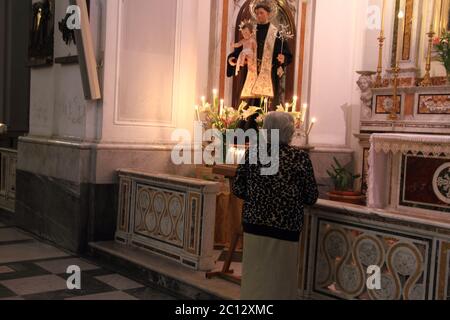 Eine ältere Frau betet vor der Statue eines heiligen in der Basilika Santa Trofimena. Stockfoto