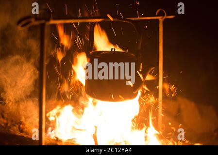 Der Wasserkocher wird nachts an einem hellen Feuer im Freien erhitzt Stockfoto