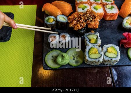 Sushi-Rolle essen mit Essstäbchen. Sushi-Set-Restaurant. Schwarzer Hintergrund. Japanisches Sushi-Essen. Gesunde Ernährung. Draufsicht. Speisenangebot. Stockfoto