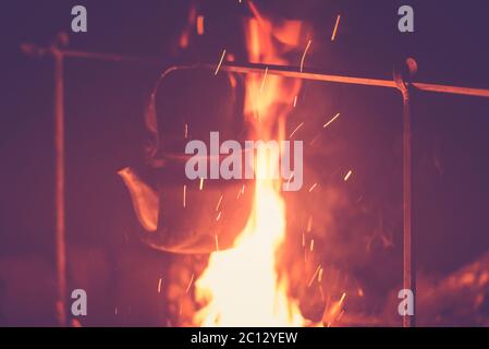 Der Wasserkocher wird auf einem hellen Feuer in der Nacht im Freien erhitzt, getönte Foto Stockfoto