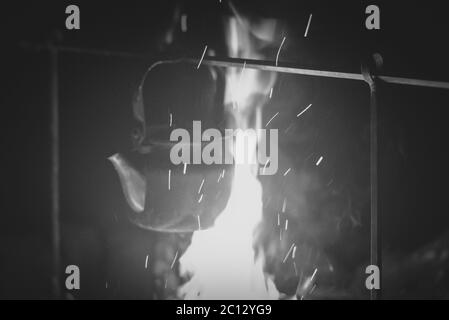 Der Wasserkocher wird auf einem hellen Feuer in der Nacht im Freien, schwarz-weiß Foto erhitzt Stockfoto