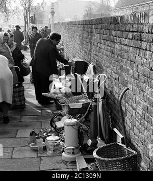 AJAXNETPHOTO. FEBRUAR 1975. PORTSMOUTH, ENGLAND. - FLOHMARKT - IN DER UNICORN ROAD; KÄUFER STÖBERN DURCH GEBRAUCHTE WAREN UND KLEIDUNG AUF DEM BÜRGERSTEIG.FOTO:JONATHAN EASTLAND/AJAX REF:7513 5 122 Stockfoto