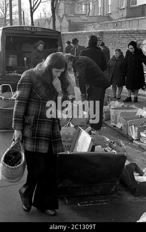 AJAXNETPHOTO. FEBRUAR 1975. PORTSMOUTH, ENGLAND. - FLOHMARKT - IN DER UNICORN ROAD; KÄUFER STÖBERN DURCH GEBRAUCHTE WAREN UND KLEIDUNG AUF DEM BÜRGERSTEIG.FOTO:JONATHAN EASTLAND/AJAX REF:7513 7 121 Stockfoto