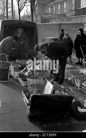 AJAXNETPHOTO. FEBRUAR 1975. PORTSMOUTH, ENGLAND. - FLOHMARKT - IN DER UNICORN ROAD; KÄUFER STÖBERN DURCH GEBRAUCHTE WAREN UND KLEIDUNG AUF DEM BÜRGERSTEIG.FOTO:JONATHAN EASTLAND/AJAX REF:7513 10 126 Stockfoto