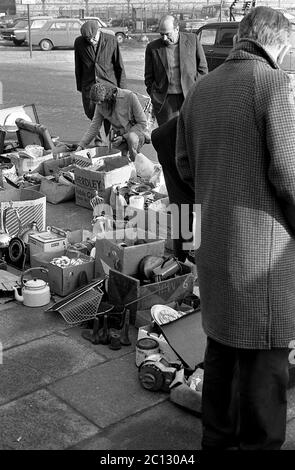 AJAXNETPHOTO. FEBRUAR 1975. PORTSMOUTH, ENGLAND. - FLOHMARKT - IN DER UNICORN ROAD; KÄUFER STÖBERN DURCH GEBRAUCHTE WAREN UND KLEIDUNG AUF DEM BÜRGERSTEIG.FOTO:JONATHAN EASTLAND/AJAX REF:7513 17 133 Stockfoto