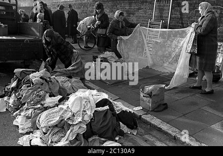 AJAXNETPHOTO. FEBRUAR 1975. PORTSMOUTH, ENGLAND. - FLOHMARKT - IN DER UNICORN ROAD; KÄUFER DURCHSTÖBERN GEBRAUCHTE WAREN UND KLEIDUNG AUF DEM BÜRGERSTEIG VERSTREUT; INSPEKTION EINES NET VORHANG.FOTO:JONATHAN EASTLAND/AJAX REF:7513 19A 119 Stockfoto