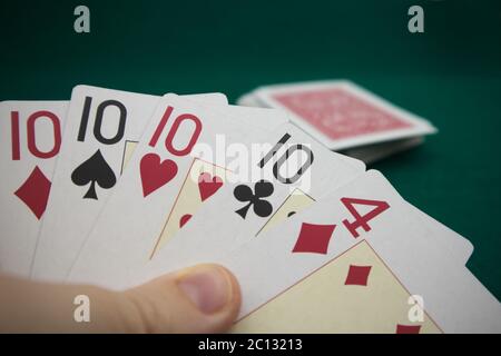 Nahaufnahme einer Kartenhand während eines Pokerspiels befindet sich im Hintergrund ein Kartenspiel auf einer grünen Spielmatte Stockfoto