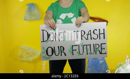 Unkenntlich Frau Aktivistin in T-Shirt mit Recycling-Logo mit protestierenden Nachricht Poster Don't Trash unsere Zukunft. Hintergrund mit Zellophanbeutel, Flaschen. Beseitigen Sie die Verschmutzung durch Plastikmüll Stockfoto