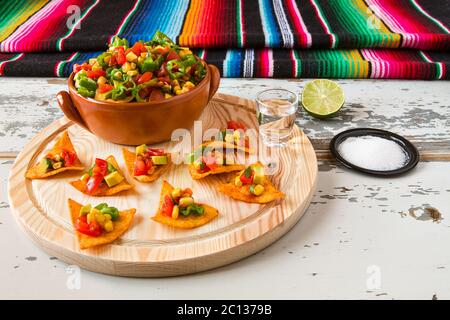 Nachos Chips und Gemüse in einem irdenen Schüssel und Tequila mit einem Poncho auf Hintergrund Stockfoto