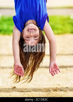 Kind hängt kopfüber auf den Affenstangen Stockfoto