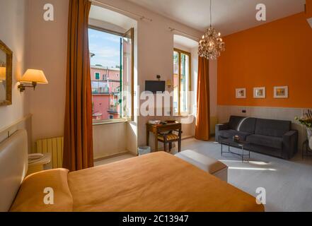 Ein helles Zimmer mit großen Fenstern und einer hohen Decke mit Blick auf ein buntes italienisches Dorf. Stockfoto