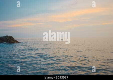 Blick vom Hafen Vernazza in Cinque Terre, Italien, während ein kleines Boot auf den Sonnenuntergang an der ligurischen Küste fährt. Stockfoto