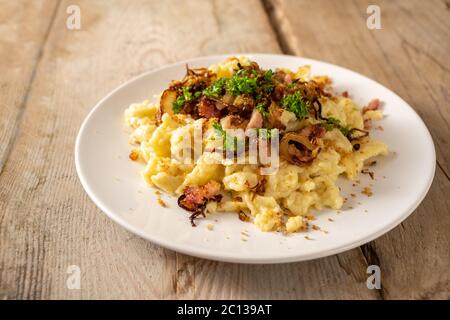 Hausgemachte Spätzle, deutsche Eiernudeln mit Käse, gebratene Zwiebeln, Speck und Paniermehl, serviert mit Petersilie garnieren auf einem weißen Teller auf einem rustikalen Woo Stockfoto