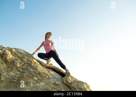 Frau Wanderer Klettern steilen großen Felsen an einem sonnigen Tag. Junge Kletterin überwindet schwierige Kletterrouten. Aktive Erholung in der Natur Konzept. Stockfoto