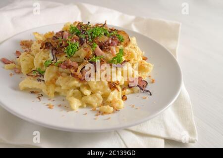 Hausgemachte deutsche Eiernudeln, genannt spätzle, mit Käse, gebratenem Speck, Zwiebeln und Paniermehl, serviert mit Petersilie garnieren auf einem Teller, Serviette und ein WH Stockfoto