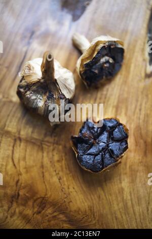 Schwarzer Knoblauch Zwiebeln und Knoblauchzehen auf hölzernen Hintergrund Stockfoto