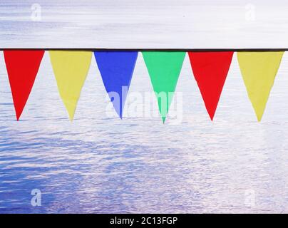 Mehrfarbige dreieckige Flaggen, die vor dem Hintergrund des blauen Flusses hängen. Stockfoto