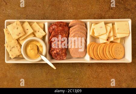 Ein rechteckiger Servierteller mit drei Fächern mit Käse, würziger Salami, Balogna, mit einem dijon-Senf. Stockfoto