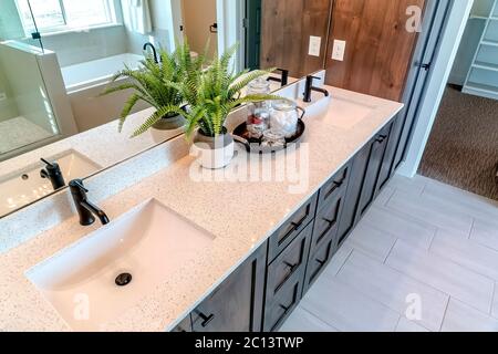 Zwei Waschbecken auf weißem Arbeitsfläche mit Pflanze neben Tablett aus Baumwolle und Seife in Gläsern Stockfoto