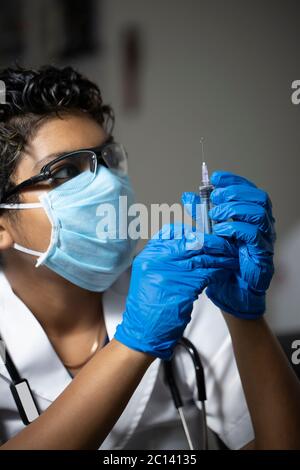 Ärztin mit einer Schutzmaske, Handschuhe und einer Spritze mit Nadel Stock Foto Stockfoto