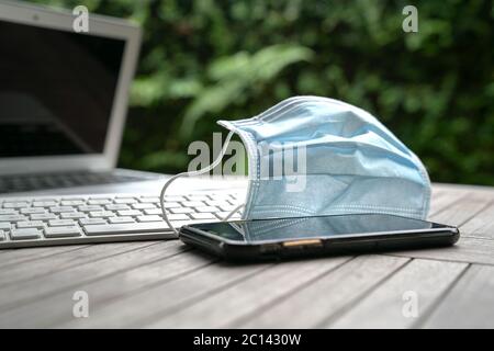 Medizinische Gesichtsmaske auf der Oberseite des Computers Laptop-Tastatur und Handy. Arbeiten zu Hause während covid-19 Konzept. Stockfoto