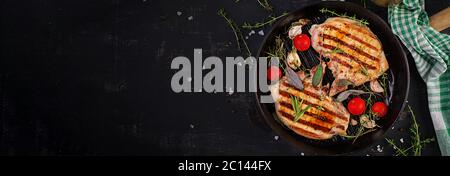 Gegrillte Schweinesteaks in Bratpfanne auf dunklem Hintergrund. Draufsicht, Banner, Kopierbereich Stockfoto