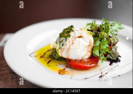 Italienischer Burrata-Käse mit Tomaten, Kräutern, Pesto und Olivenöl. Stockfoto