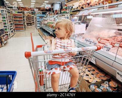 Budva, Montenegro - 10. juni 2020: Ein einjähriges Mädchen sitzt in einem Supermarkt-Trolley in der Fleischabteilung. Stockfoto