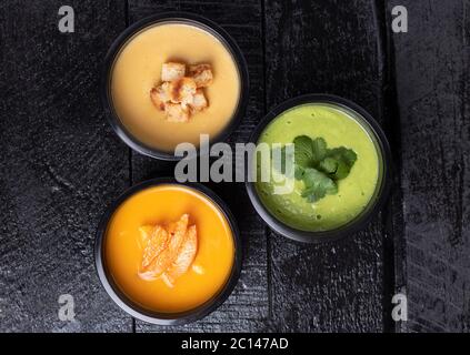 Bunte vegane Cremesuppe in schwarzen Futterschachteln, flach liegend. Ausgewogene Ernährung Konzept. Lieferung von Lebensmitteln Stockfoto