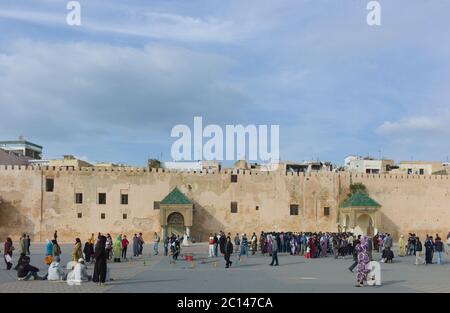 Ein Überblick über den Platz und die Stadtmauer mit arabischen Menschen, die auf dem Platz nahe der Stadtmauer in Meknes, Marokko, spazieren. Blauer Himmel Stockfoto