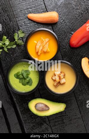 Spinatcremesuppe, Kürbis- und Avacado-Suppen in Lebensmittelbehältern, flach legen. Holzhintergrund, vertikal Stockfoto