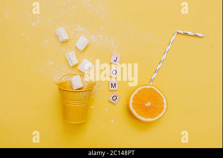 Abkürzung Wort JOMO geschrieben auf Holz umweltfreundliche Buchstaben und festliche Cocktail-Tube in saftig reifen Orange und Marshmallows aus einem kleinen gelben buc Stockfoto