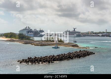 Nassau, Bahamas - 3. Mai 2019: Blick auf den Leuchtturm in Nassau, Bahamas und Kreuzfahrtschiffe im Hafen bei bewölktem Wetter. Wellenbrecher im Vordergrund. Stockfoto