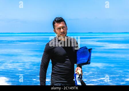 Junger Inder mit Schnorchelausrüstung, der auf den Malediven aus dem Wasser läuft Stockfoto