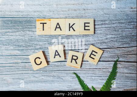 Schriftzug Take Care ist aus kleinen Holzblöcken auf einem Holzhintergrund mit einem grünen frischen Blatt von Grün gedruckt. Medical Ready-made modernen conte Stockfoto