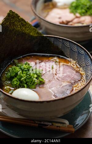 asiatische Ramen mit Schweinefleisch Nudeln Schnittlauch Brühe Ei und Nori auf einer traditionellen Schüssel mit bunten flachen Hintergrund Stockfoto